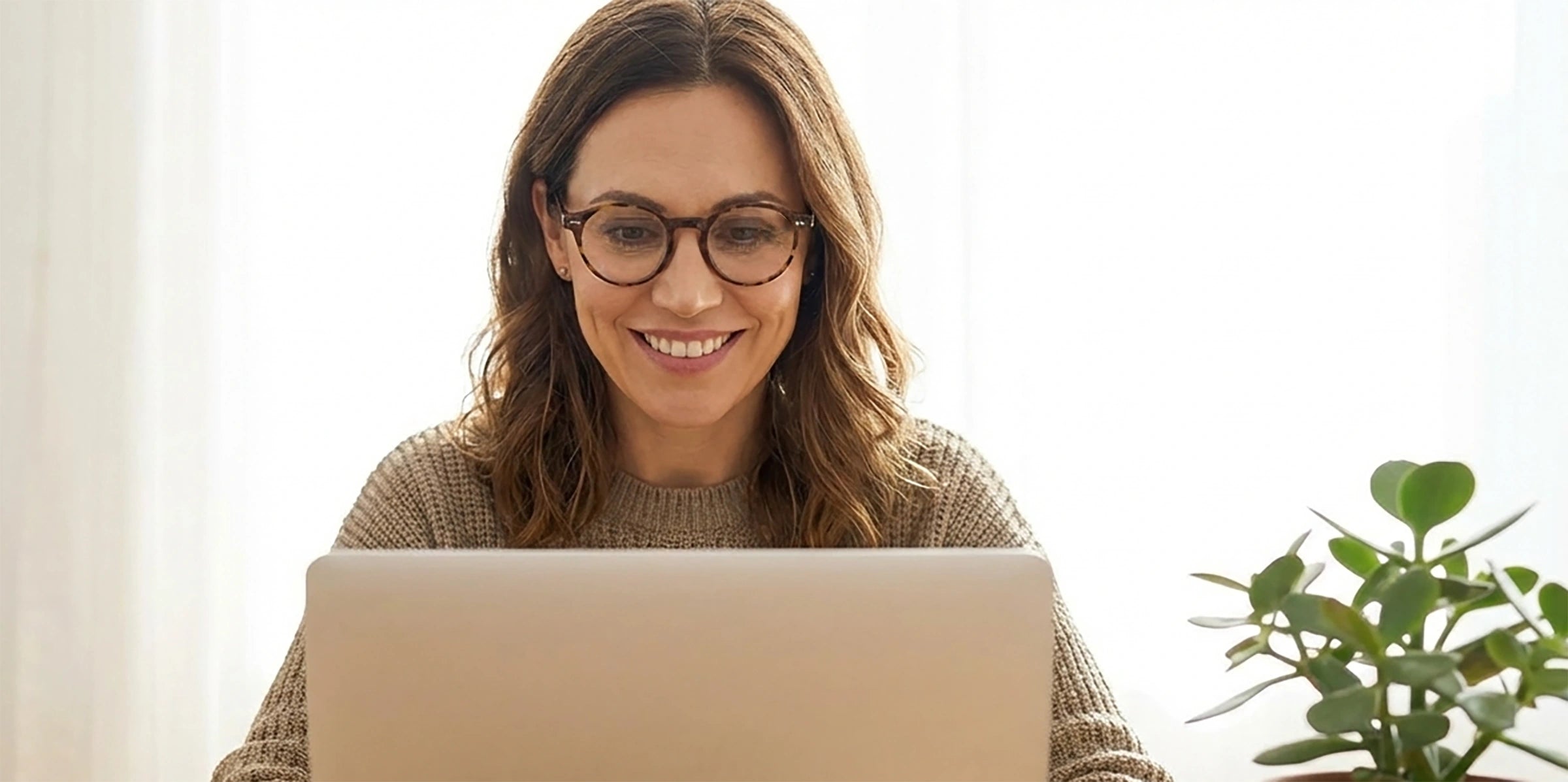 Woman wearing computer glasses using a laptop with a plant in the background